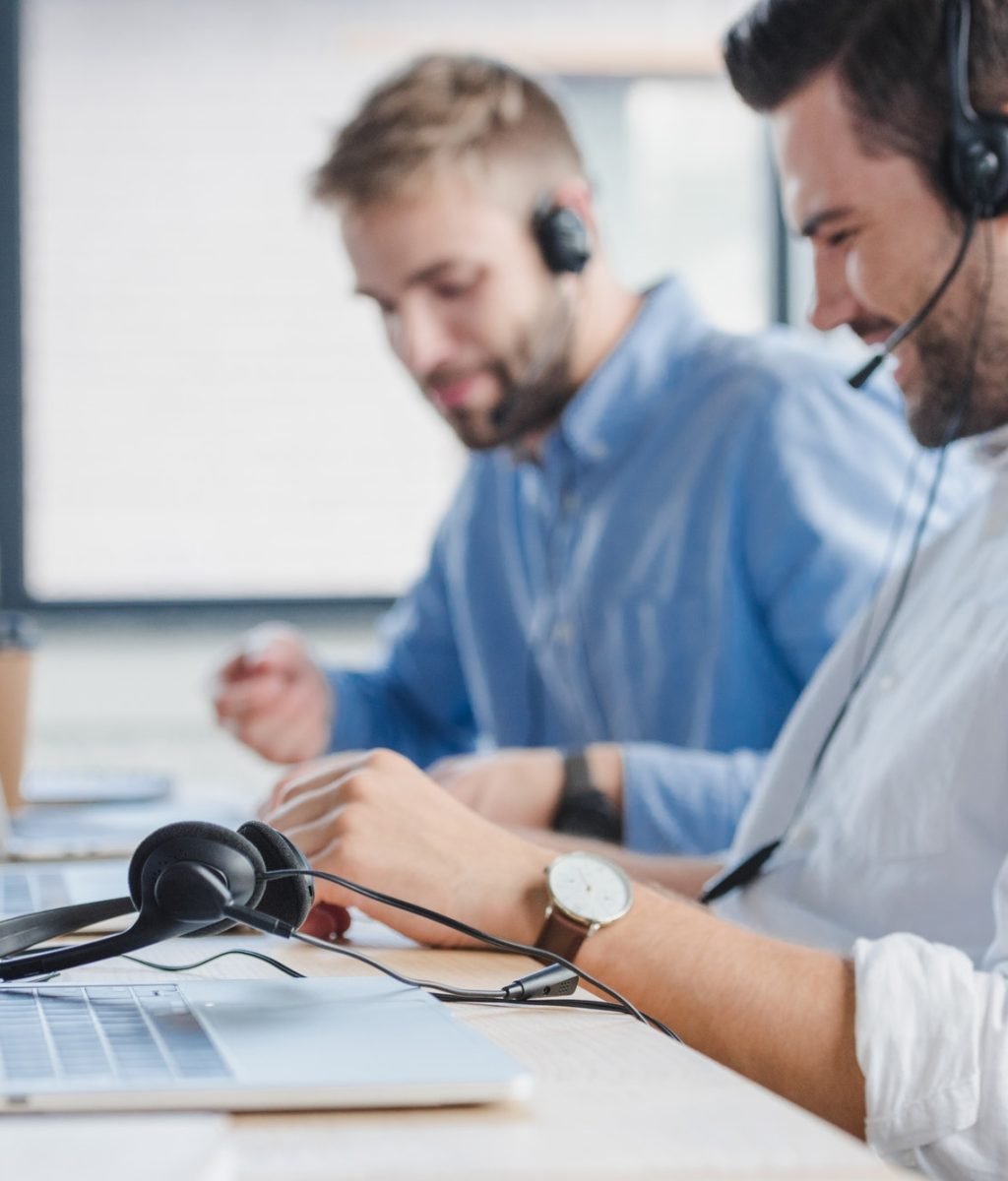 smiling-young-call-center-operators-in-headsets-using-laptops-in-office.jpg